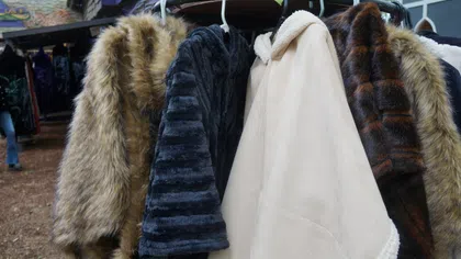Various fur and faux fur coats hanging on a rack outdoors at a market or fair.